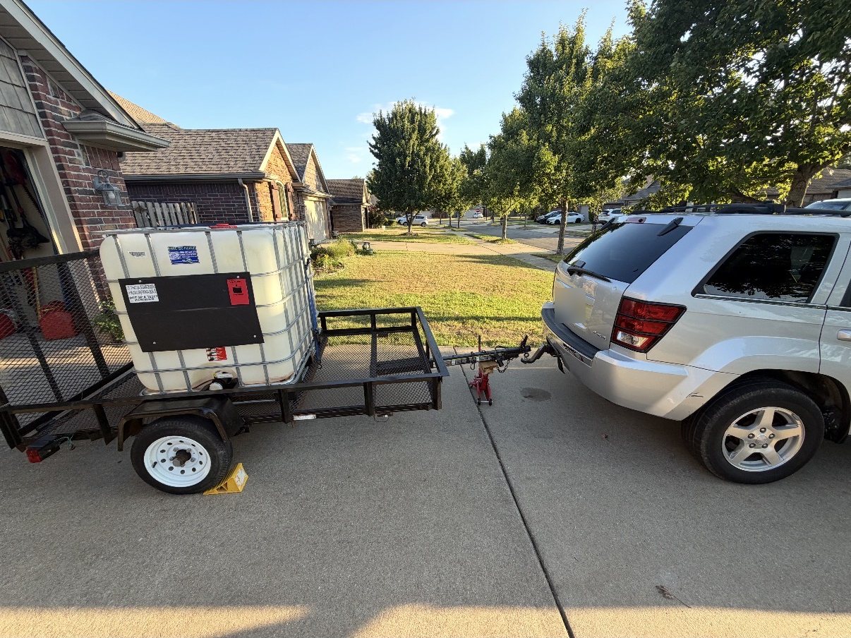 The Wash It Wash It trailer with its water tank, hitched and ready in a Fayetteville driveway